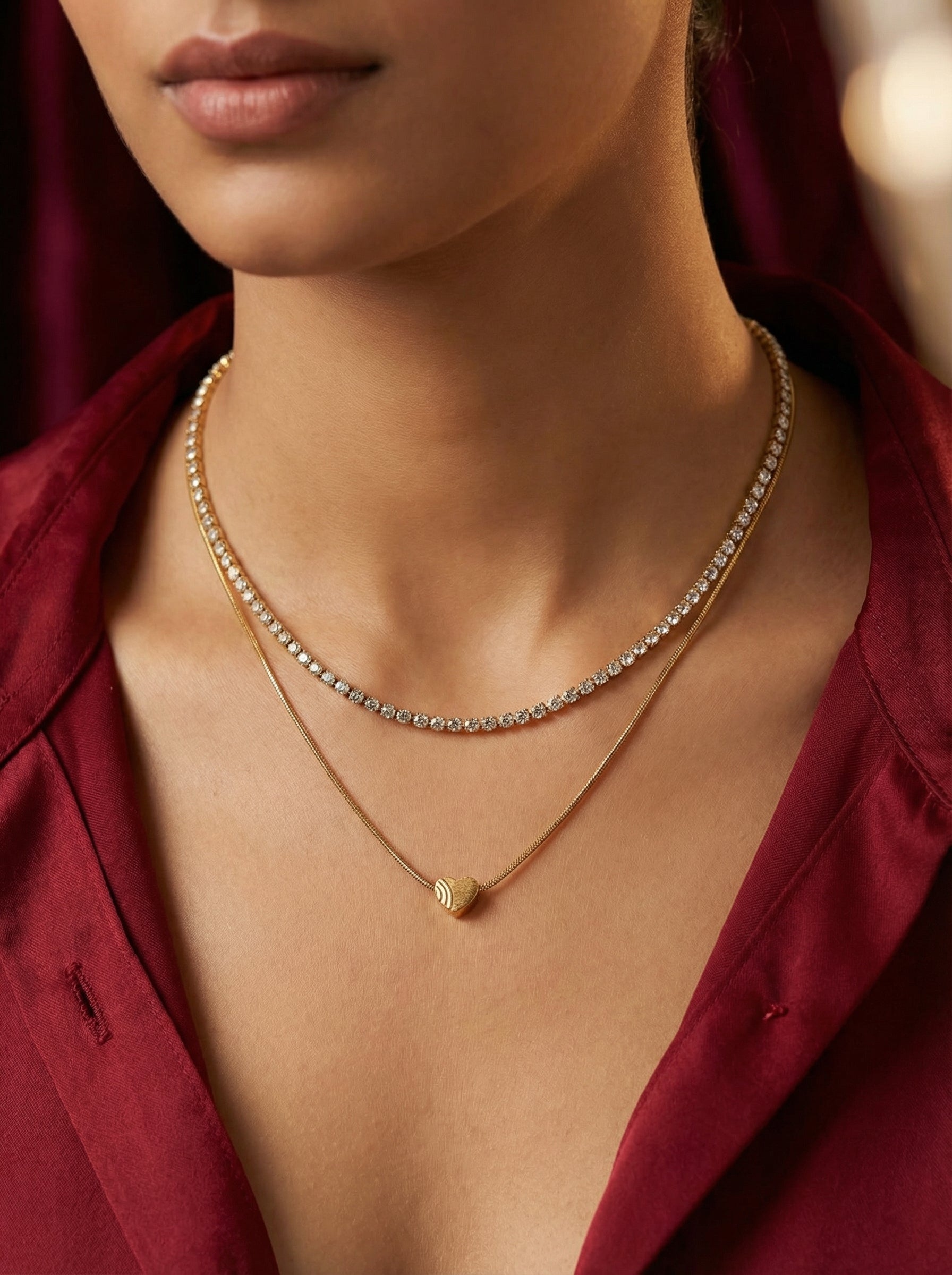 Close-up of a person wearing a gold necklace with a heart pendant against a blurred background.