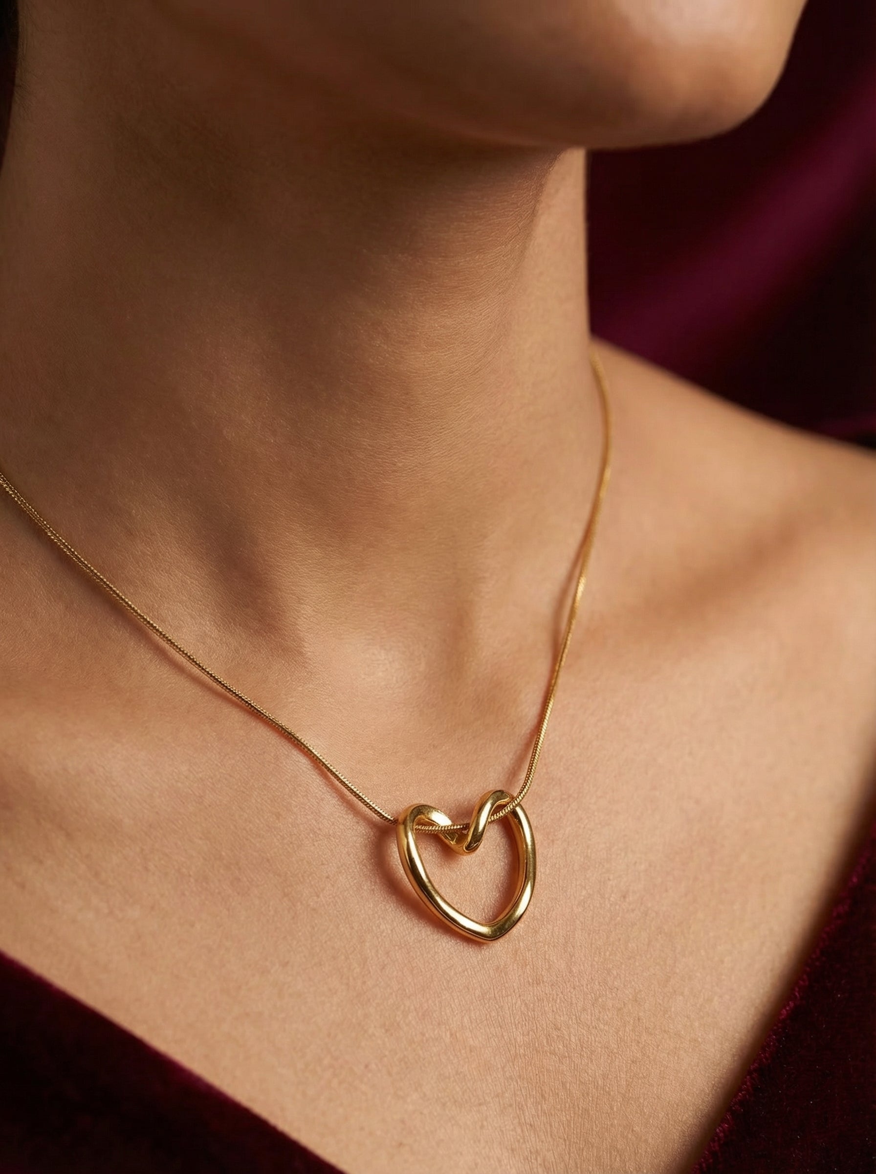 Gold heart-shaped necklace on a person's neck against a dark background