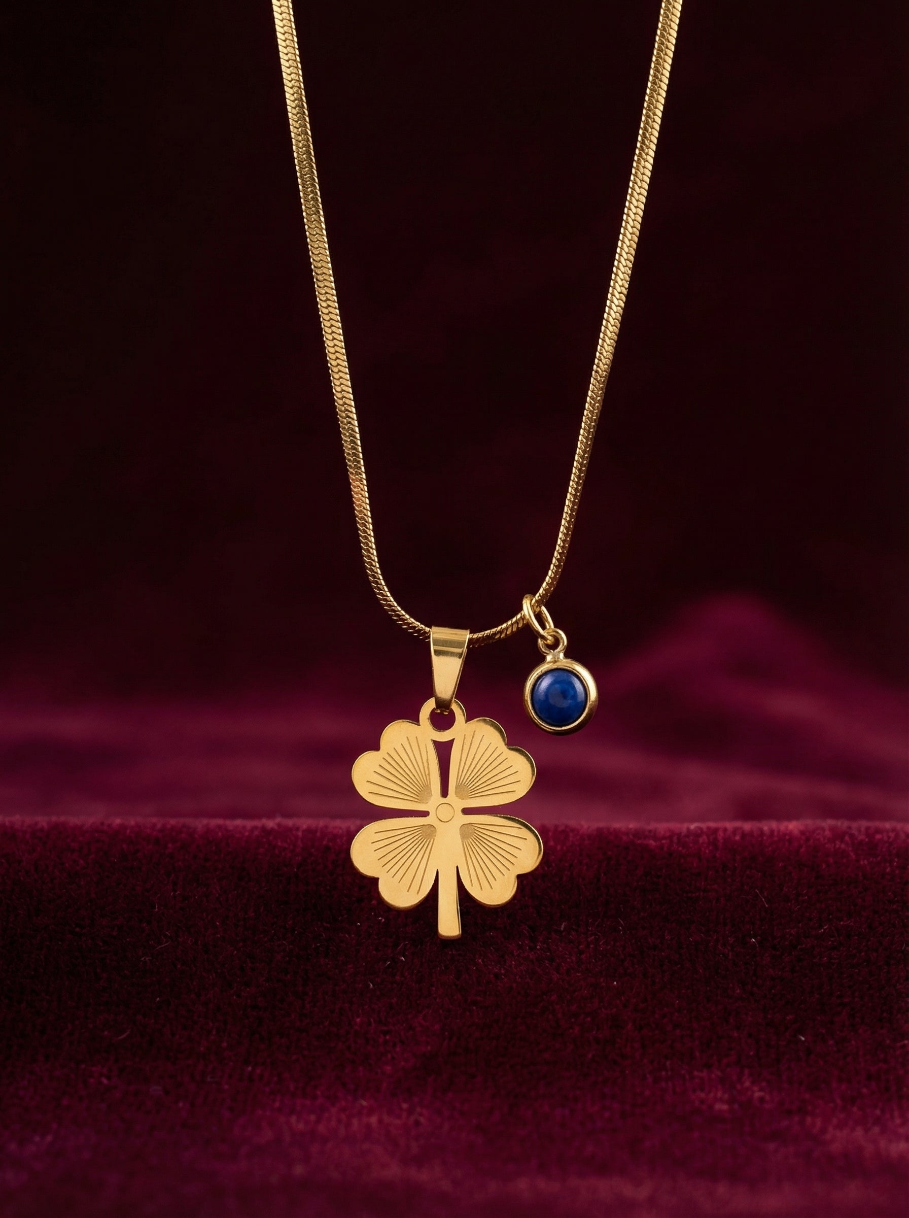 Gold necklace with a four-leaf clover pendant and blue gemstone on a dark background