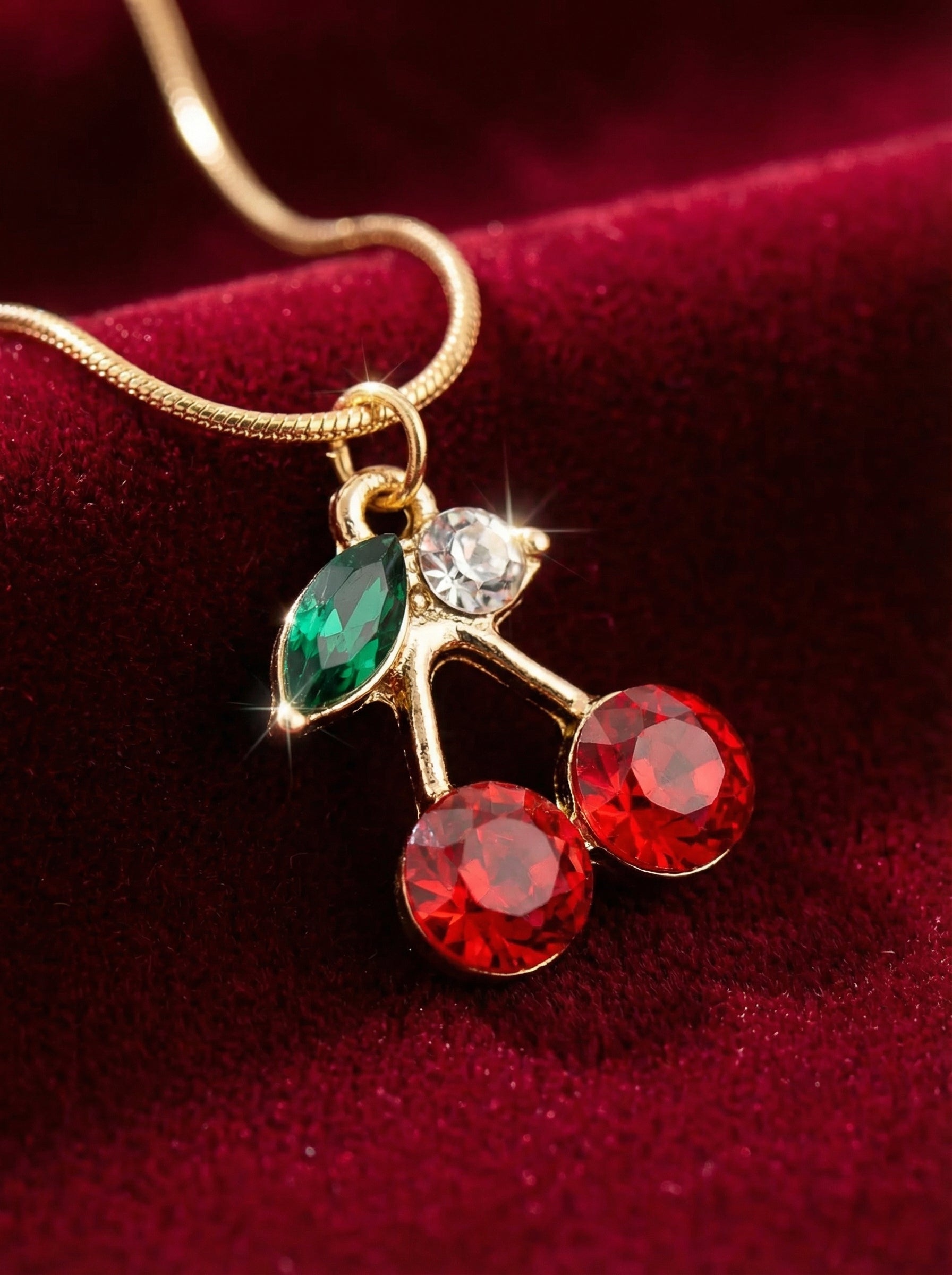 Necklace with a cherry pendant featuring red and green gemstones on a red background