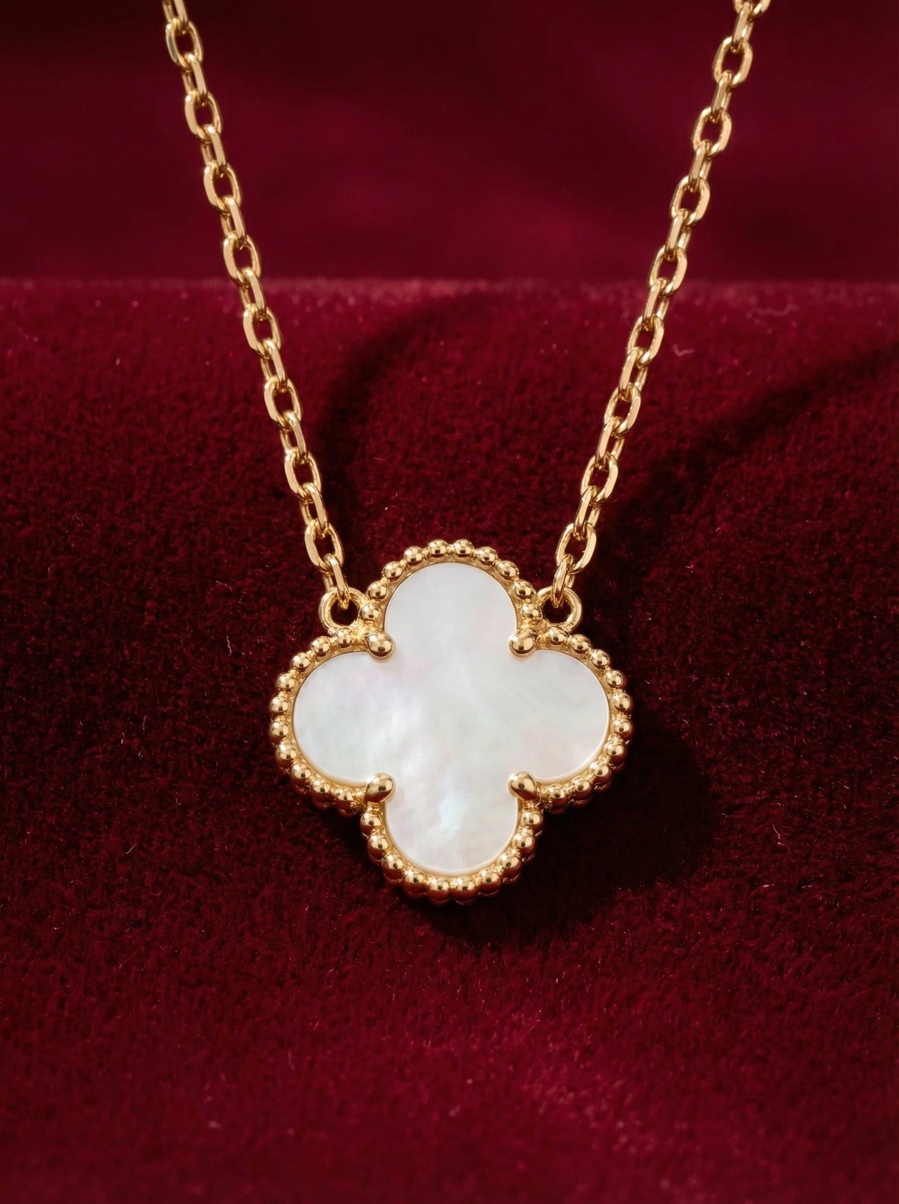 Gold necklace with a four-leaf clover pendant on a red background
