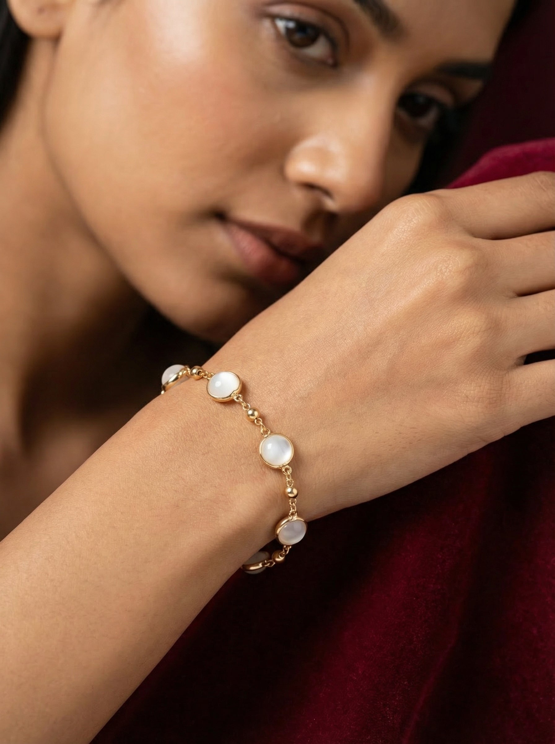 Woman wearing a gold bracelet with pearl-like stones on a blurred background