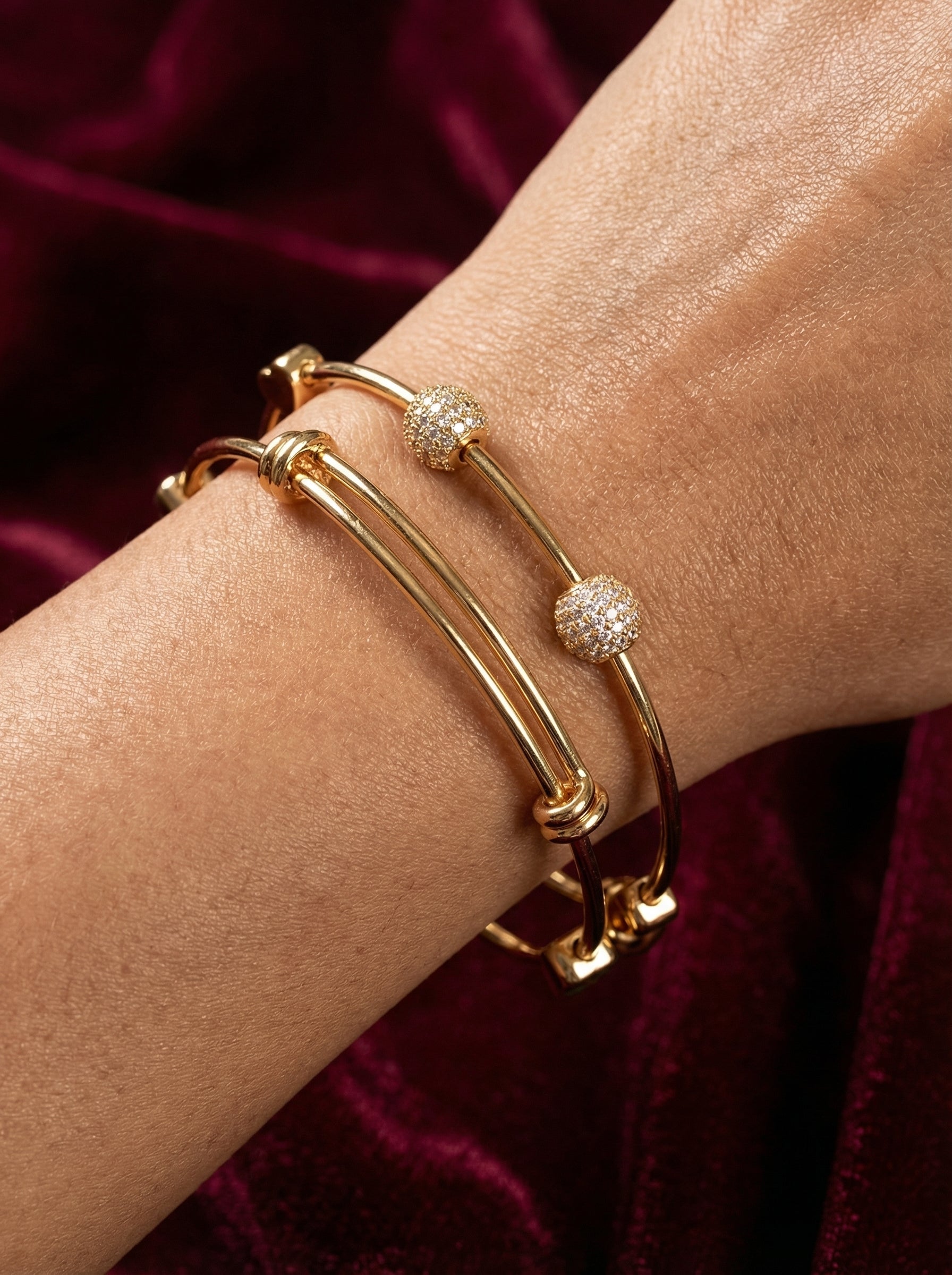 Gold bracelet with diamond accents on a wrist against a dark red fabric background