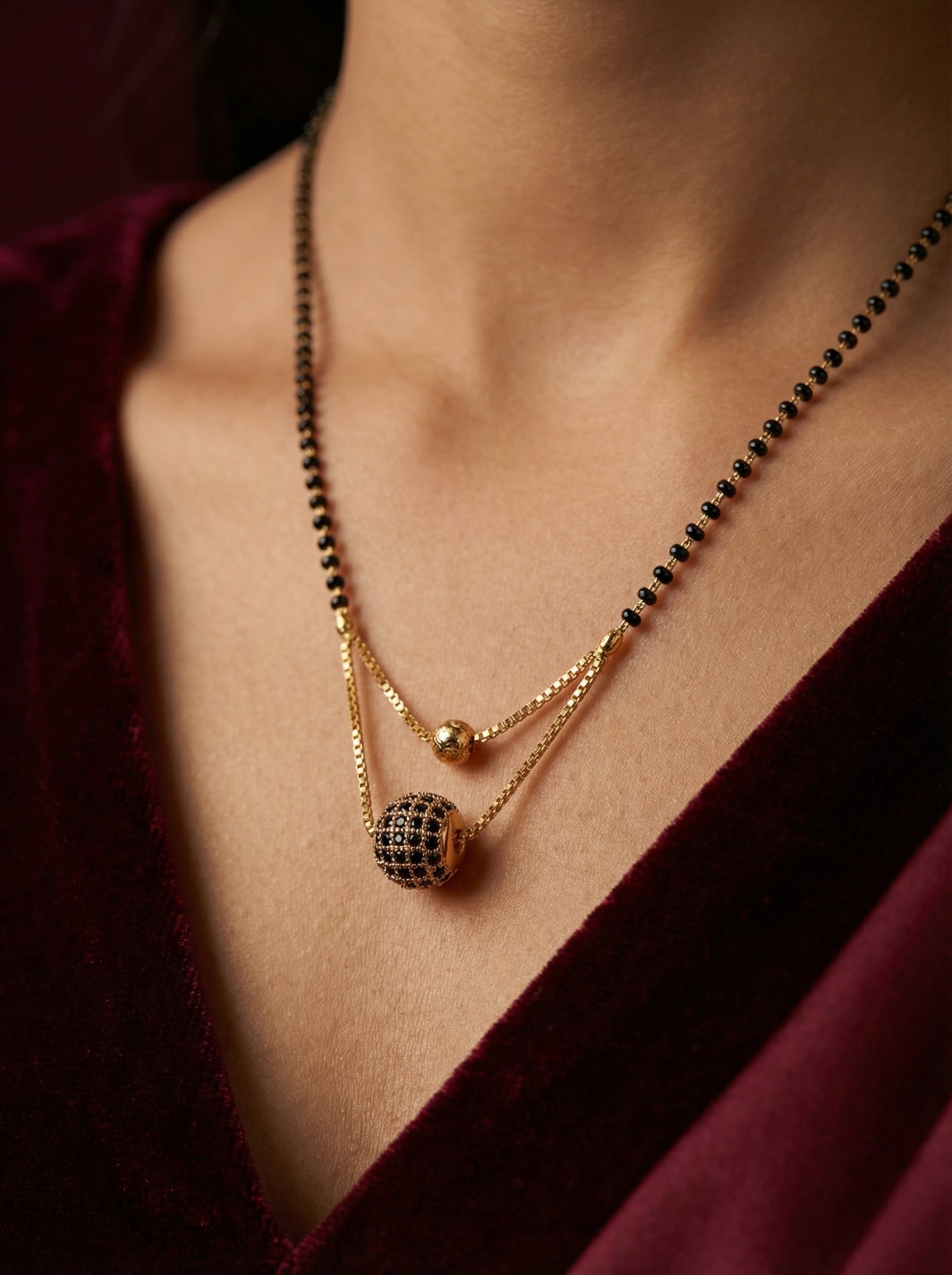 Close-up of a person wearing a gold necklace with black beads against a dark background