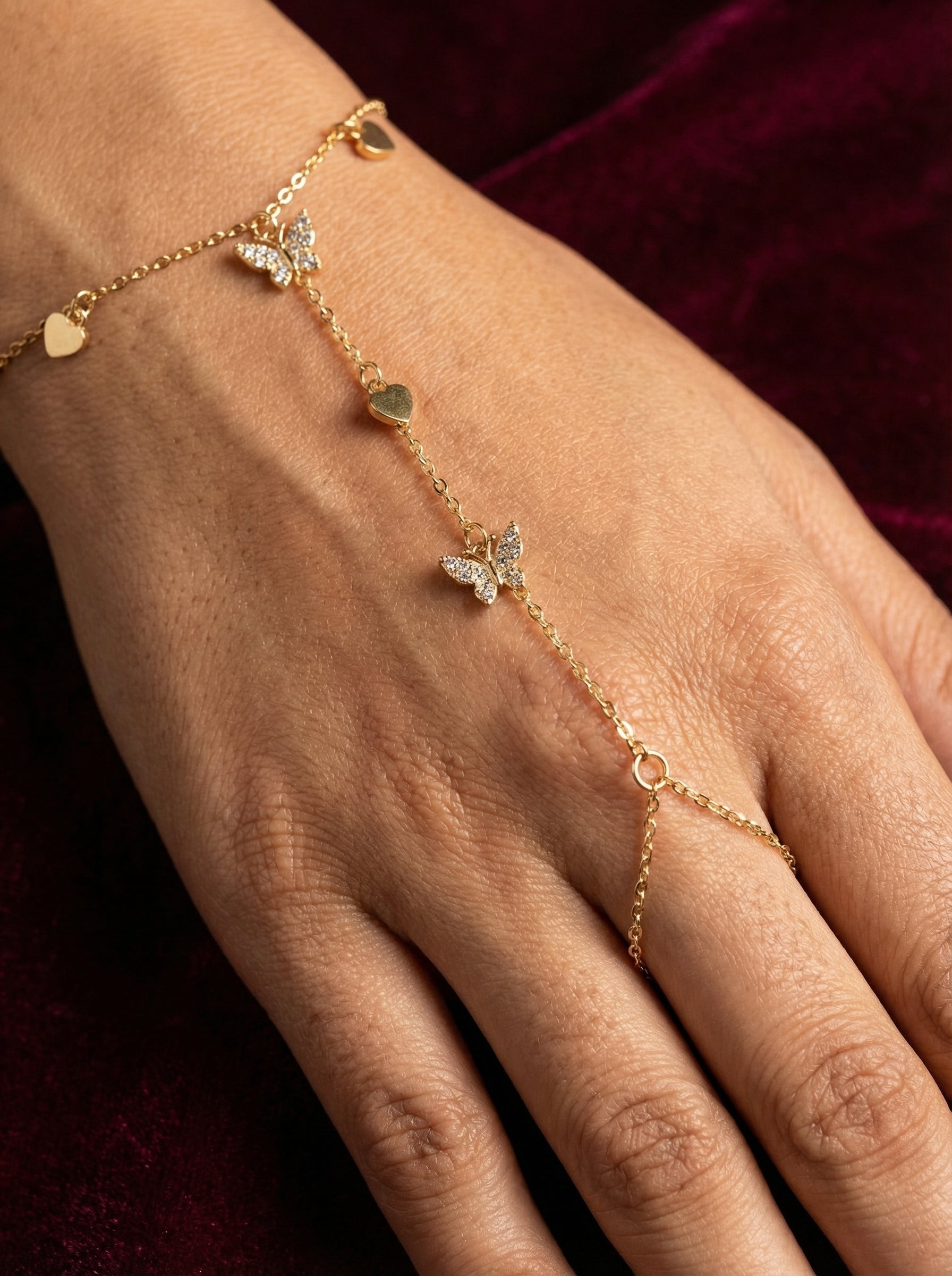 Gold bracelet with butterfly and heart charms on a hand against a dark background