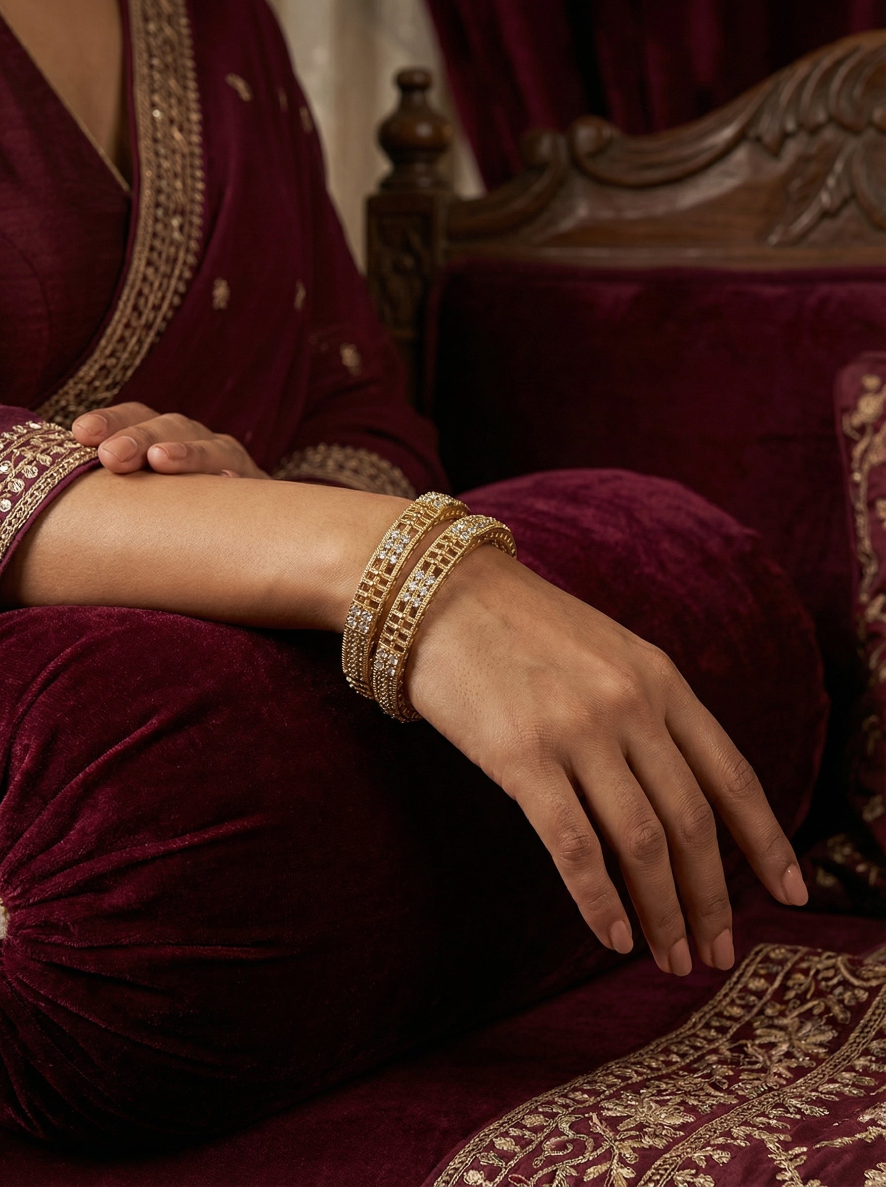 Hand wearing a gold bracelet on a maroon fabric background