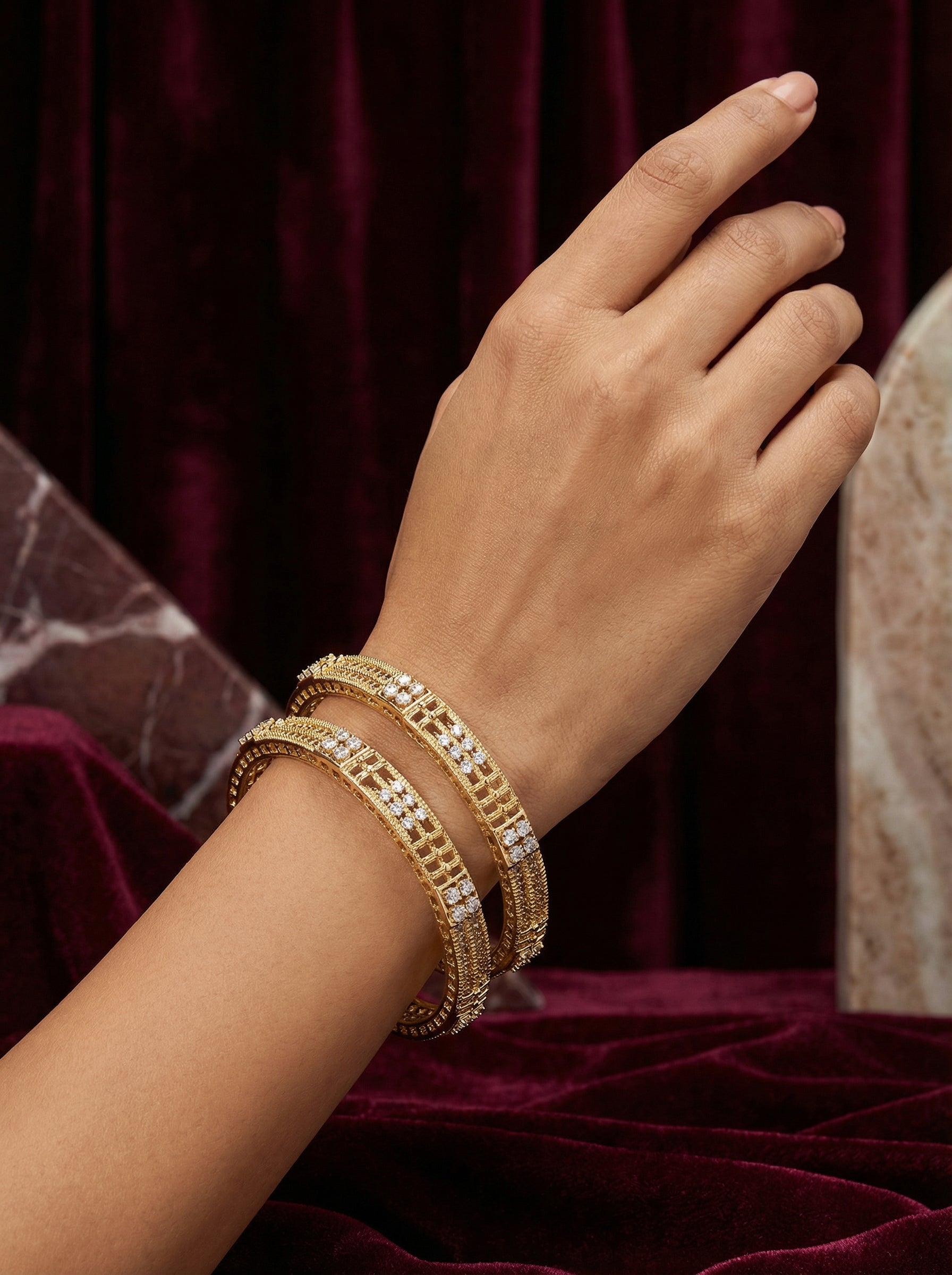 Hand wearing multiple gold bracelets on a maroon fabric background