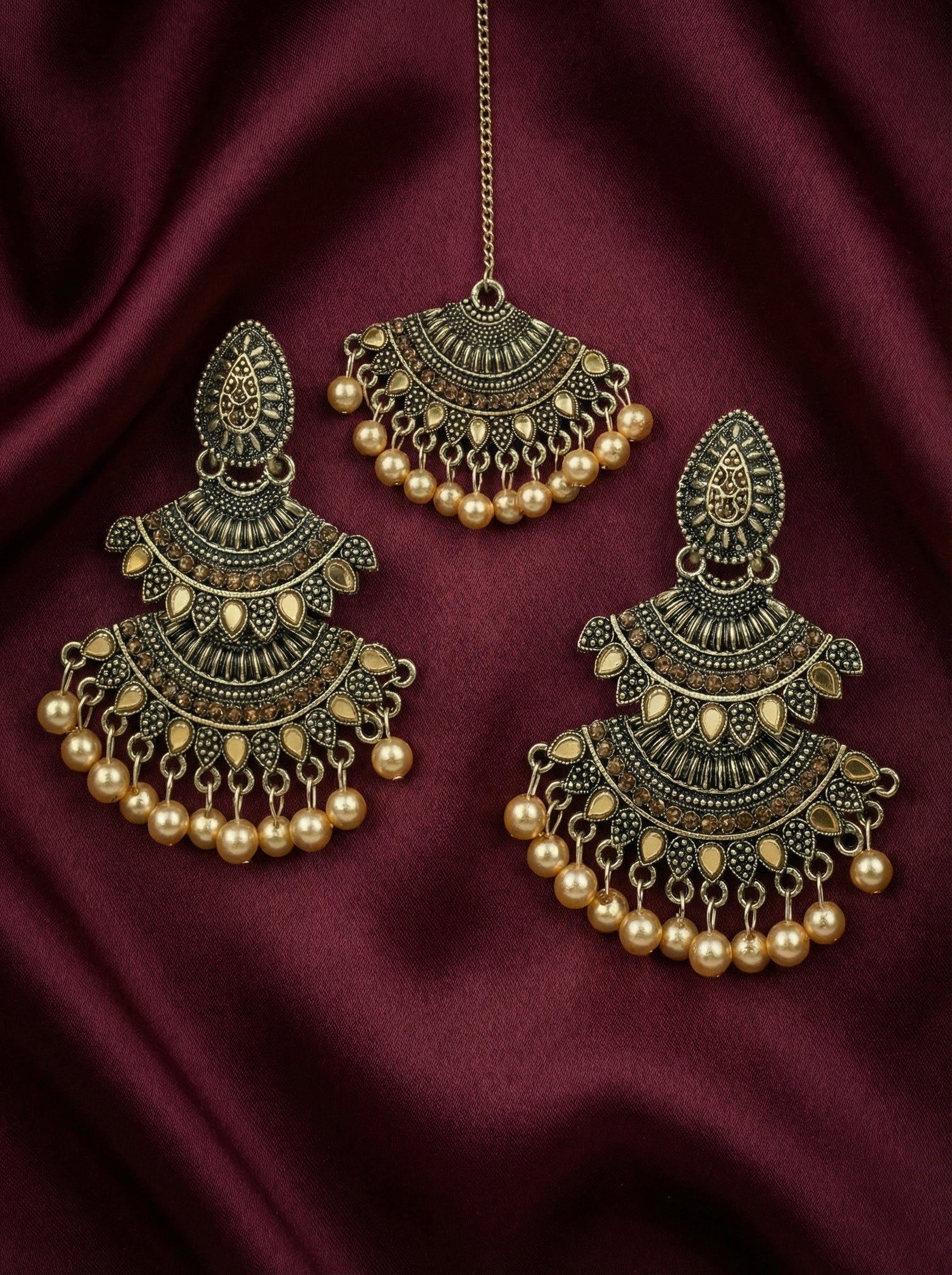 Ornate gold earrings with pearl accents on a dark red fabric background