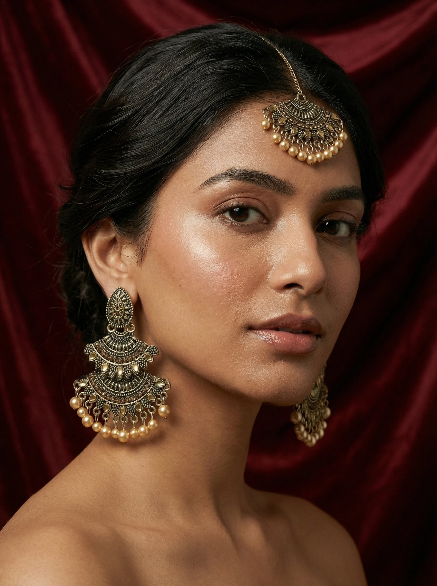 Woman wearing gold earrings against a red curtain background