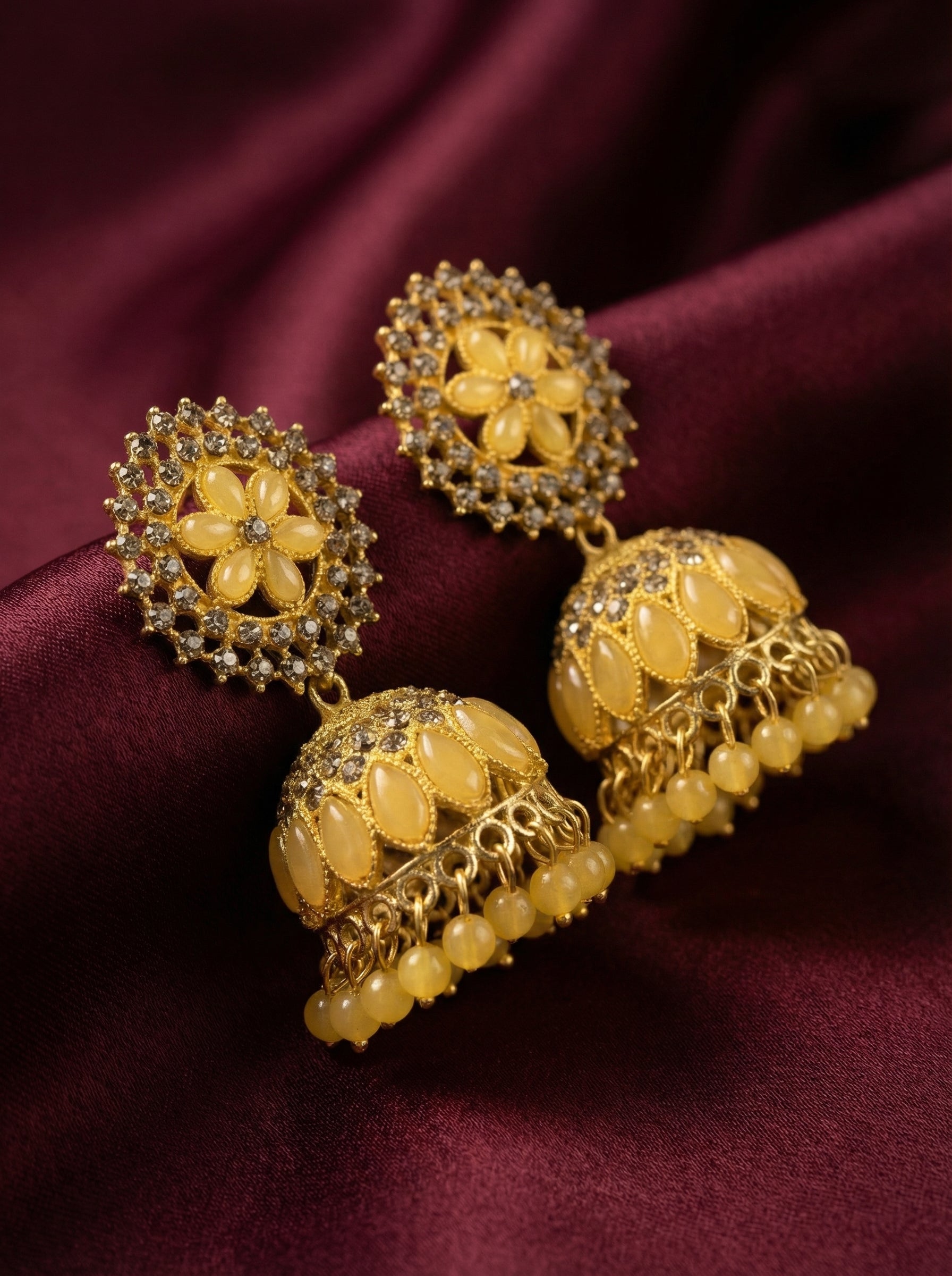 Gold and yellow earrings on a maroon fabric background