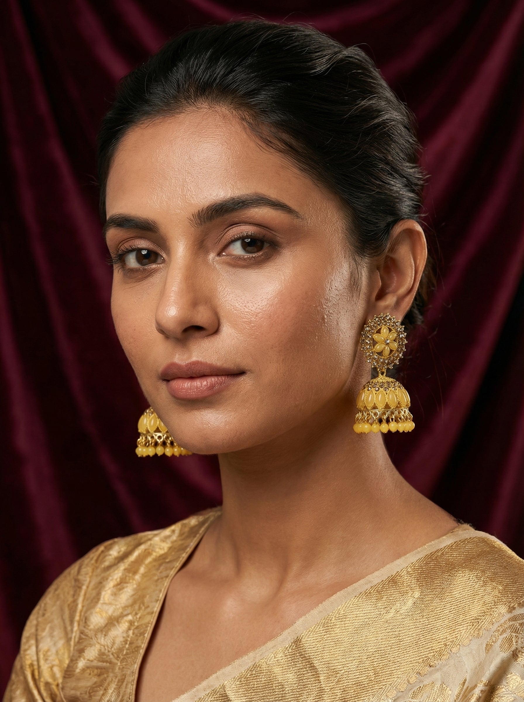 Woman wearing gold earrings and a saree against a red curtain background