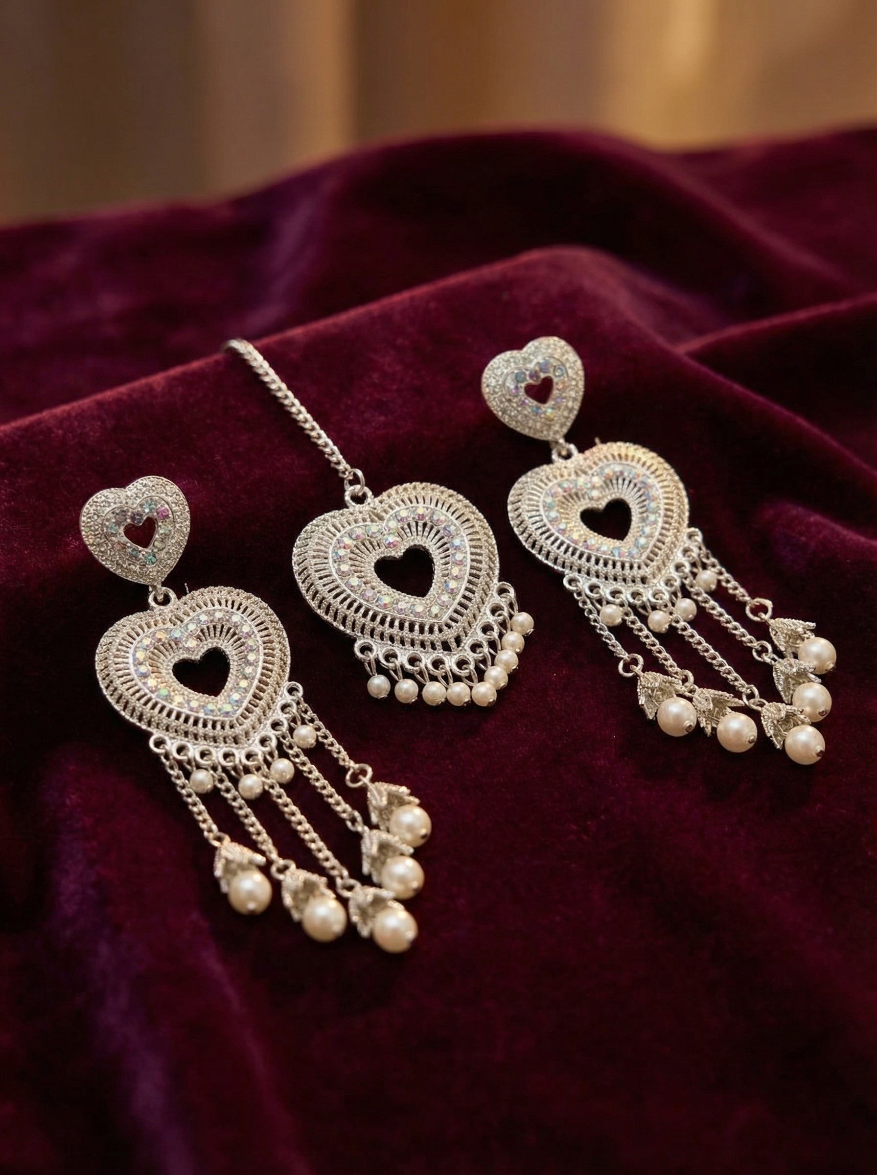 Pair of silver heart-shaped earrings with dangling beads on a burgundy fabric background