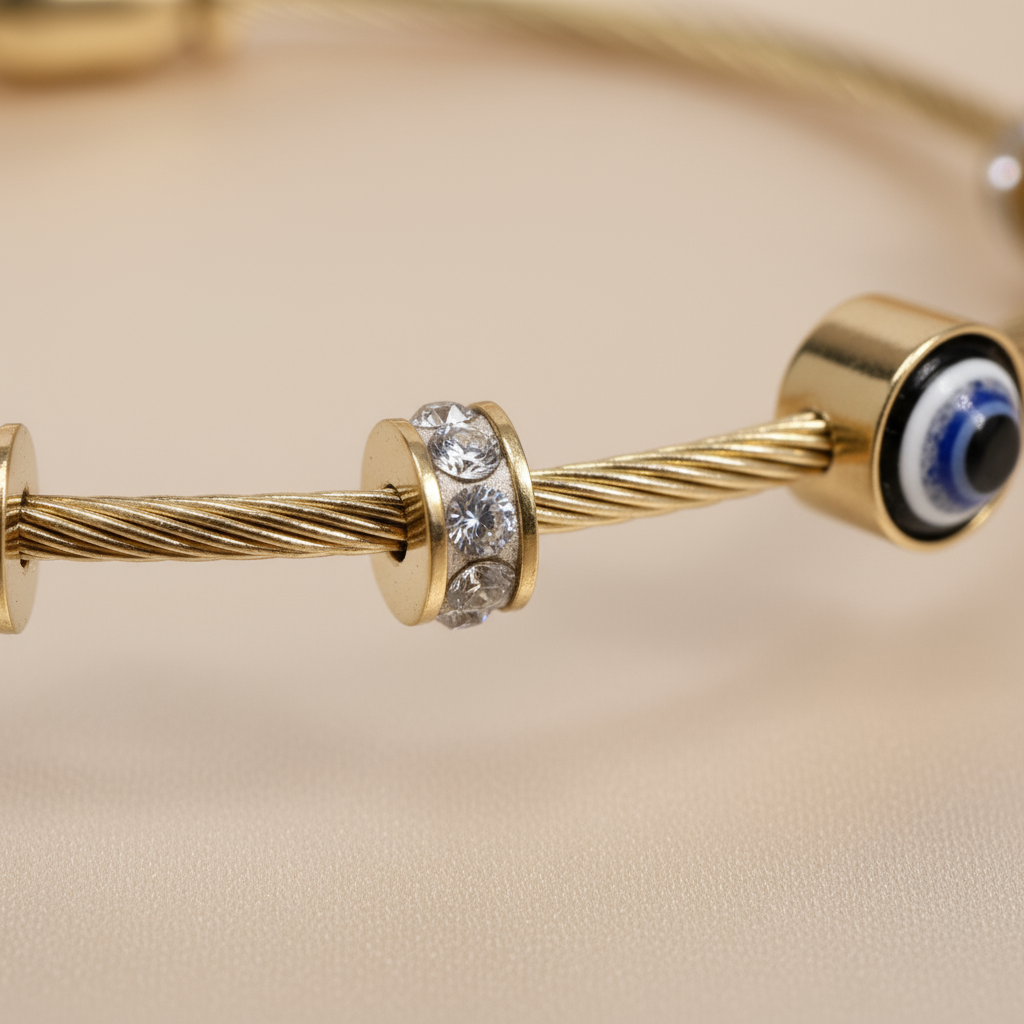 Extreme macro closeup focusing on the intricate texture of the gold cable wire band, the pavé crystal accent bead, and the enamel blue Evil Eye charm.