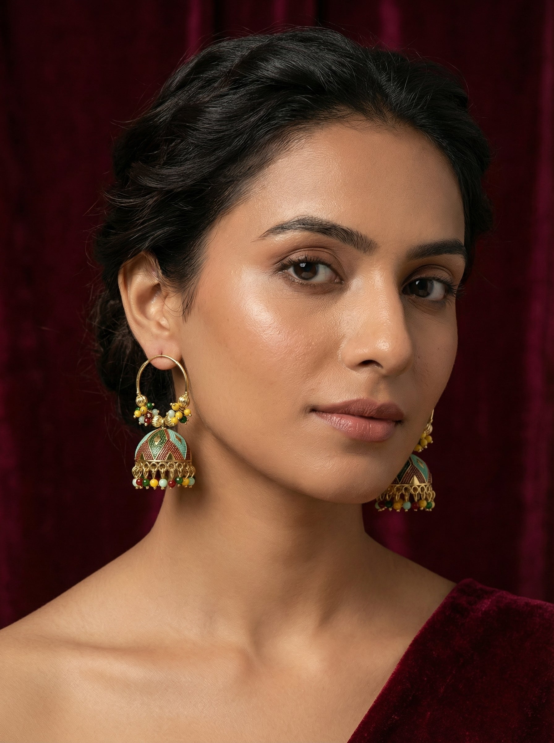 Woman wearing gold earrings with a maroon background