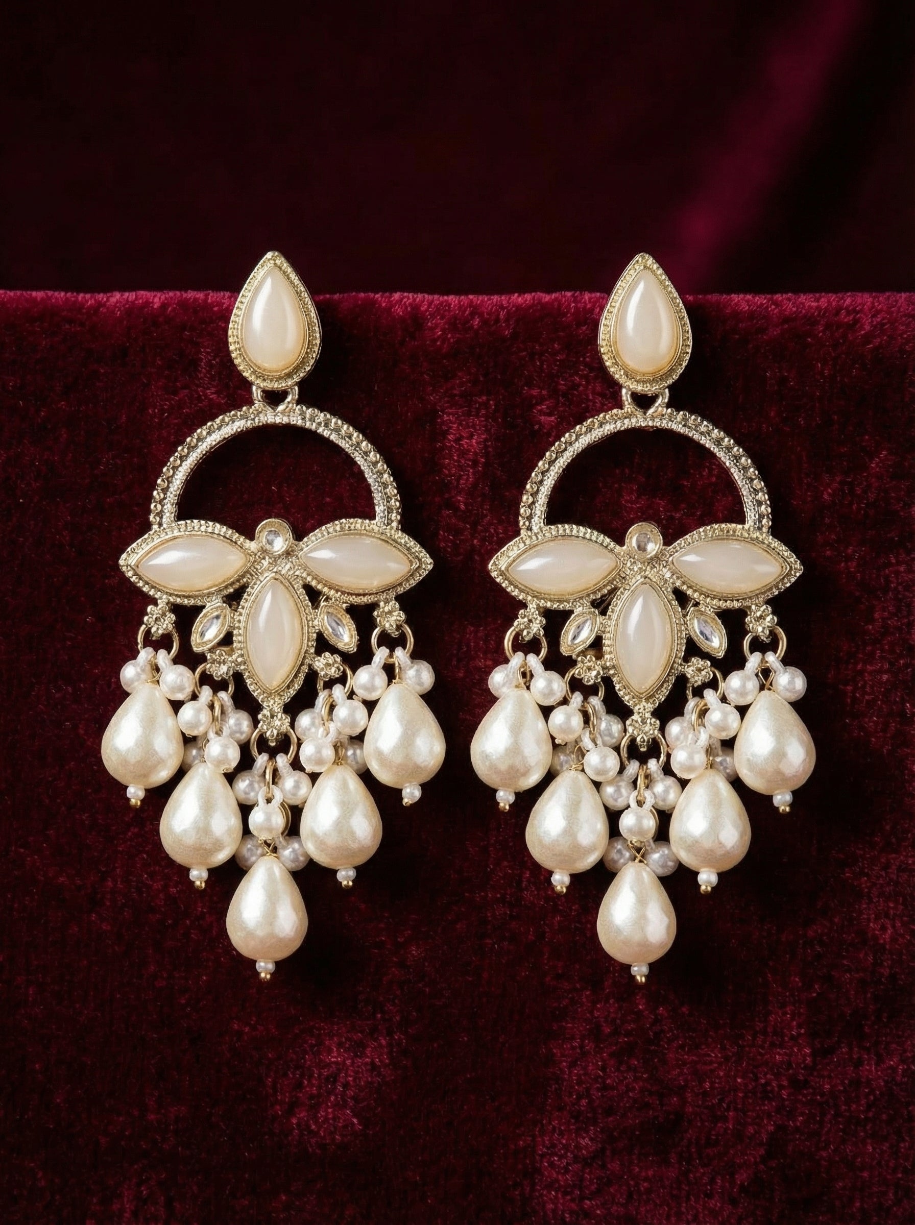 Pair of ornate earrings with pearls on a dark red background