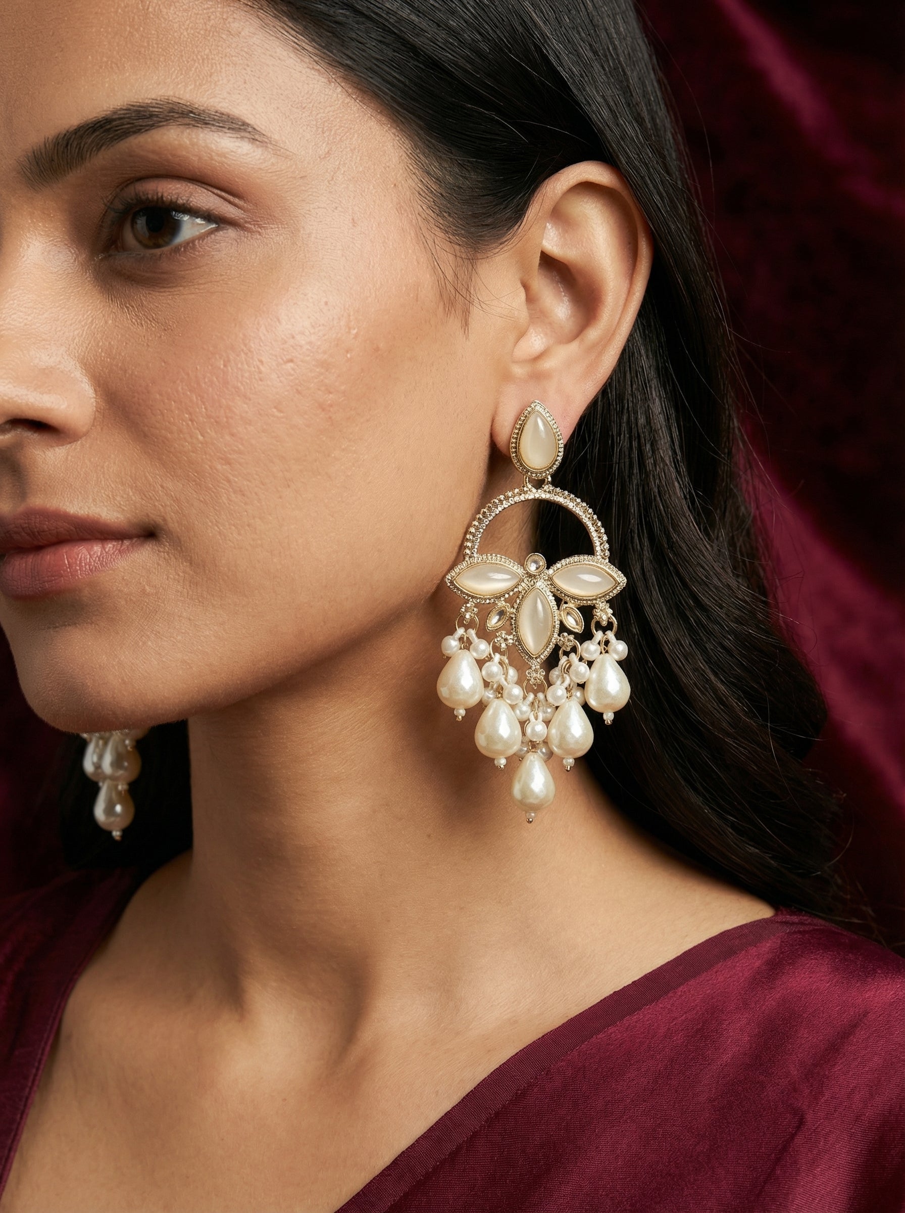 Woman wearing a pair of earrings with a maroon background