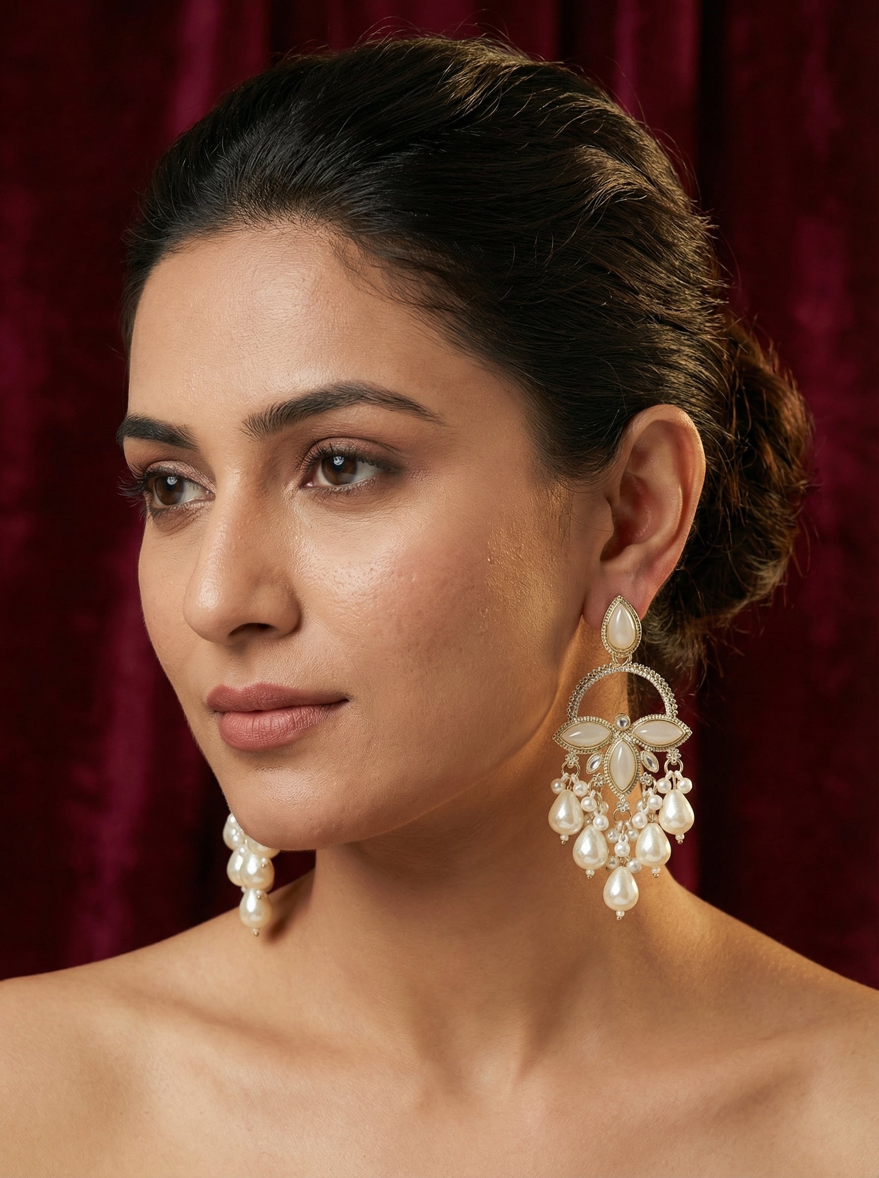 Woman wearing large, ornate earrings against a red curtain background