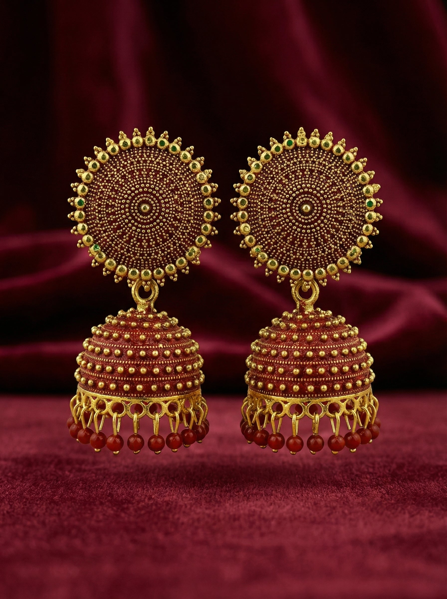Pair of gold and red beaded earrings on a maroon background